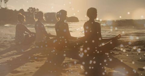 Four women meditating on surfboards at sunset beach silhouettes, golden hour calm