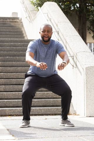 Fit african man squatting on urban stairs exercising with smartwatch and athletic wear