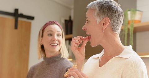 Senior and middle-aged women tasting snacks while laughing in cozy modern kitchen