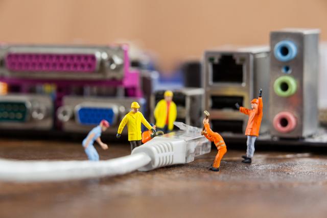 This visual captures miniature engineers and workers seemingly connecting a LAN cable to a computer, emphasizing teamwork and attention to detail in technology and networking setups. Perfect for use in articles and promotions related to IT industry, network management, and technological innovations. A great visual representation for blogs, advertisements, and educational materials discussing connectivity, infrastructure, and IT services.