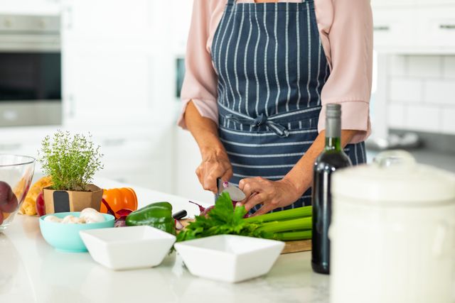 Midsection of caucasian senior woman chopping vegetables while cooking at home. unaltered, lifestyle, domestic life, retirement, food, cooking, preparation.