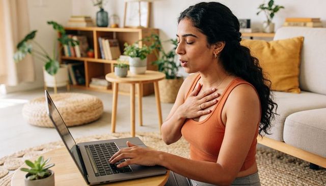 Indian woman practicing breathwork during virtual wellness session in cozy bohemian room