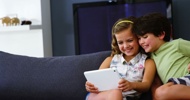 Smiling Siblings Using Tablet on Sofa - Download Free Stock Images Pikwizard.com