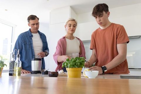 Family preparing fresh meal at modern kitchen island with teen using lemon and basil