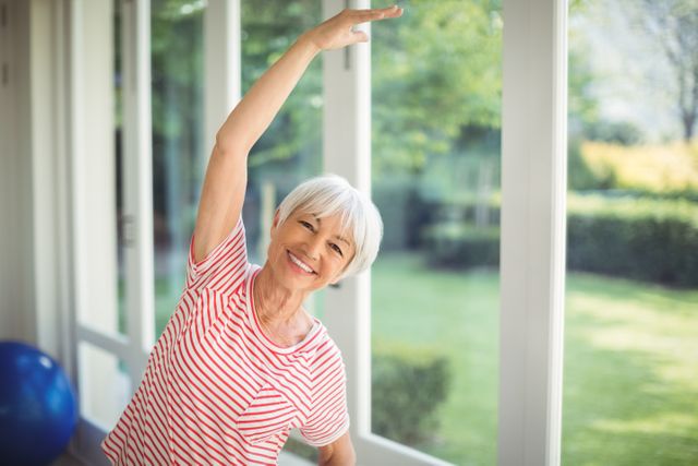 Portrait of happy senior woman performing stretching exercise at home