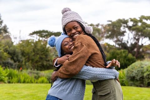 African american friends hugging and smiling in park wearing knit pom-pom hats