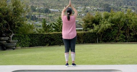 Mature woman practicing yoga poolside on patio facing lawn and garden