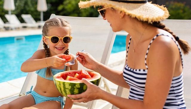 Mother and daughter sharing watermelon by poolside on sunny summer day