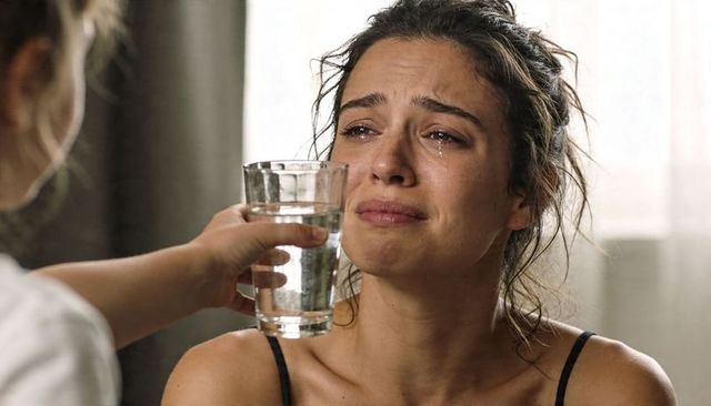 Tearful woman receiving glass of water from caring hand, intimate emotional support scene