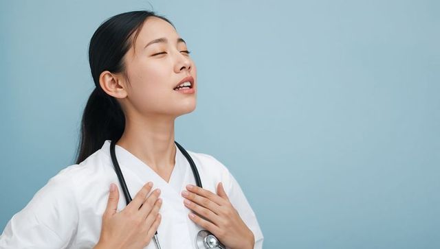 Calm nurse taking deep breaths, hands on chest, wearing white scrubs and stethoscope