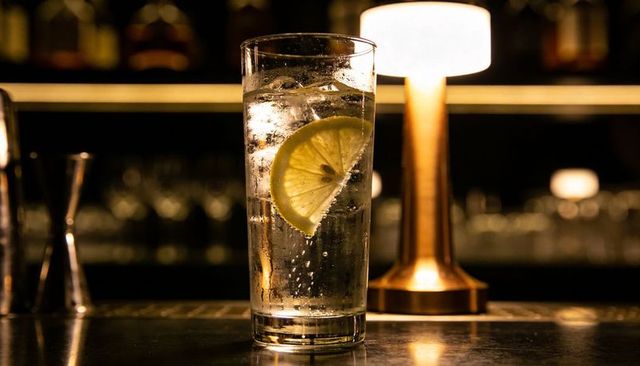Sparkling highball glass with lemon slice and warm lamp glow on bar counter