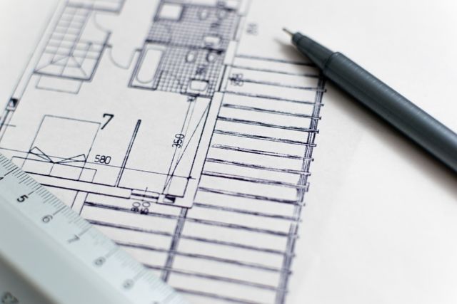 Depicts detailed architectural blueprint with pen and ruler, ideal for engineering, construction presentations, architectural workshops, educational materials on design and planning, and showcasing architectural project development.