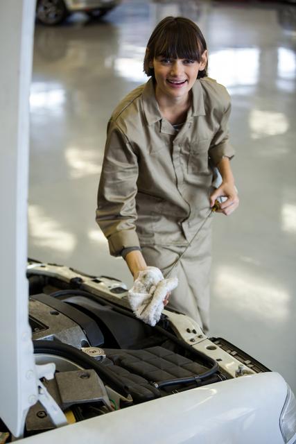 Female mechanic checking oil level with dipstick under car hood in repair garage. Ideal for automotive industry content, car maintenance tutorials, and service center advertisements.