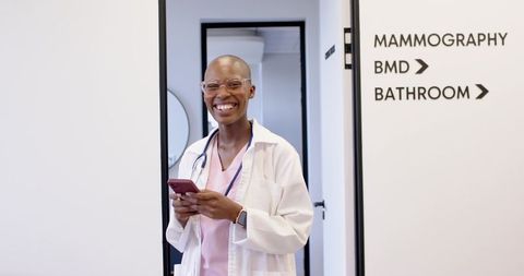 Smiling female medical professional in clinic using smartphone near mammography signage