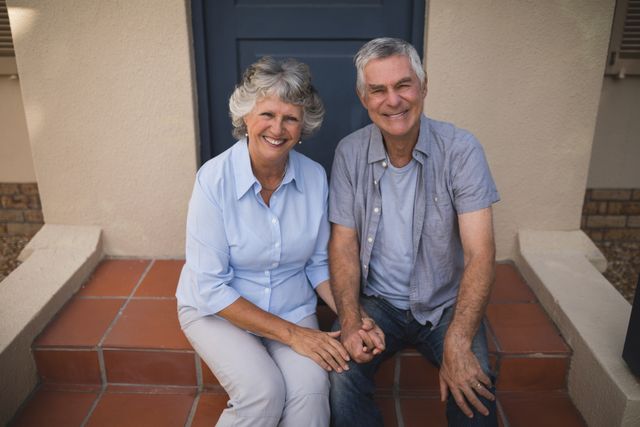 Portrait of smiling senior couple sitting together against entrance on house