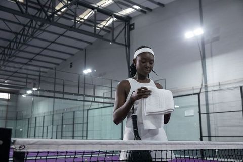 Female tennis player taking towel break on indoor purple court wearing white headband
