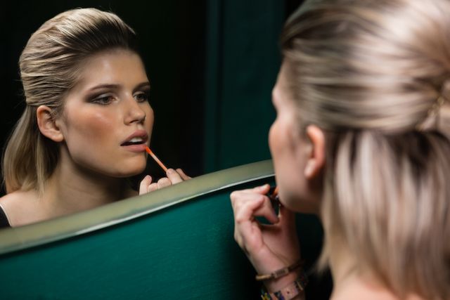 Woman applying lips gloss while looking at mirror in washroom