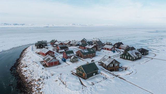 Forming arctic peninsula village with colorful wooden cabins on snowy seawall