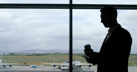 Traveler holding coffee engaged with smartphone at airport
