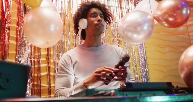 Image of happy african american male dj playing music and talking in microphone at a nightclub. Fun, inclusivity, going out and party concept.