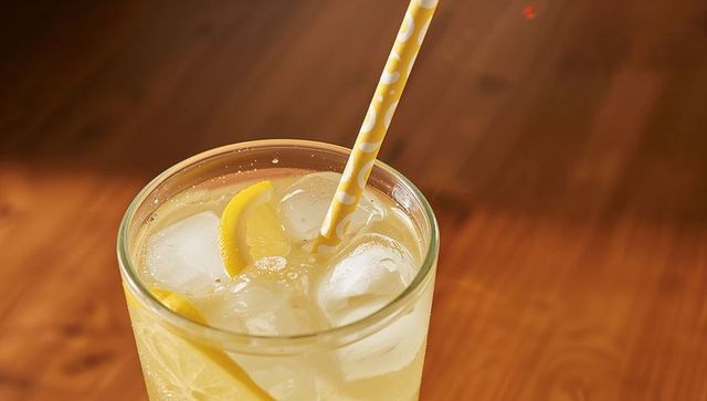 Refreshing lemonade glass showing ice, lemon slices and yellow polka dot straw on wooden table