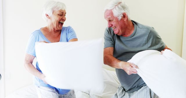 Smiling couple having pillow fight on bed in bedroom