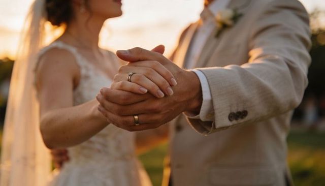 Bride and groom holding hands showing wedding rings at golden hour garden