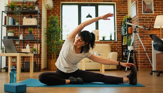 Home yoga stretching session on blue mat in bright brick living room for fitness