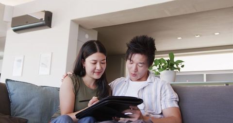 Young couple sharing tablet on couch using stylus for home planning and digital collaboration