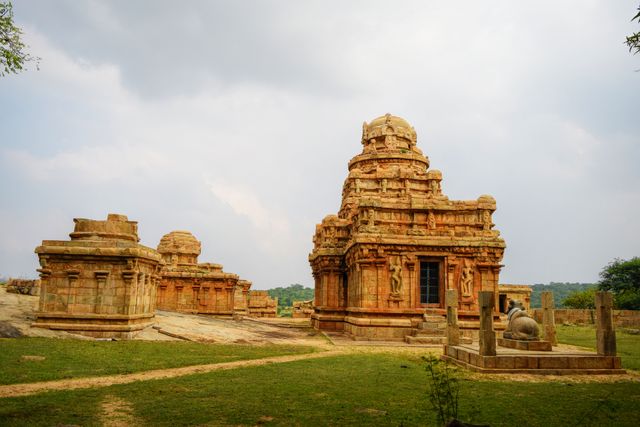 Depicting an impressive ancient Indian temple with intricately carved sandstone, this image brings to life the rich architectural heritage of South India. Set against a backdrop of a cloudy sky, it captures the serene and historic ambiance of the sacred site. Ideal for use in cultural presentations, educational materials about Indian history, travel brochures, and websites promoting heritage tourism.
