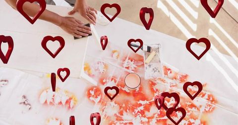 Sanding canvas on paint-splattered table with hands and floating red heart overlays