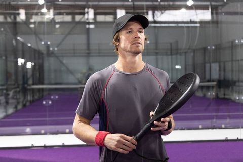 Padel player preparing for serve on indoor purple court with glass walls and focused gaze
