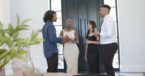 Diverse friends socializing in elegant foyer holding wine glasses during cocktail gathering