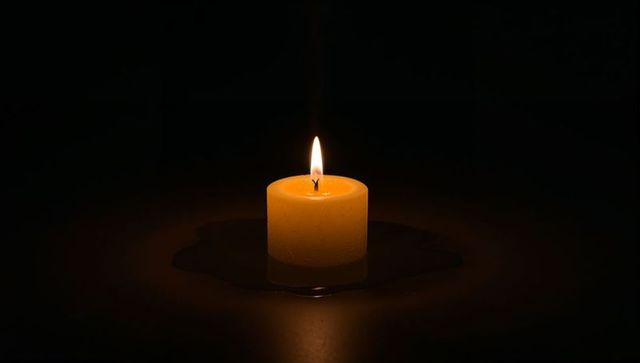Warm glowing yellow pillar candle melting into wax pool on dark reflective surface, serene ambiance