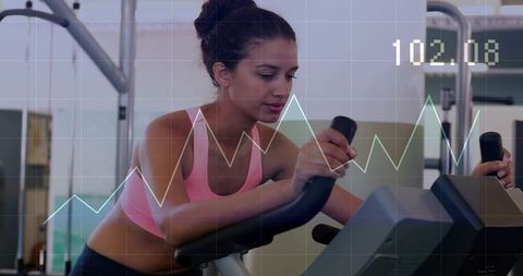 Woman checking stationary bike console with cardio analytics overlay at gym