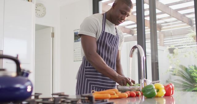 Image of happy african american man washing vegetables. Lifestyle and spending time at home concept.