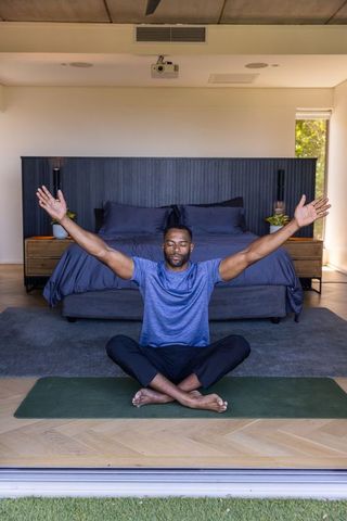 African american man meditating on yoga mat in contemporary bedroom practicing mindfulness