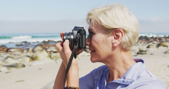 Senior hiker woman taking pictures using digital camera on the beach. trekking, hiking, nature, activity, exploration, adventure concept.