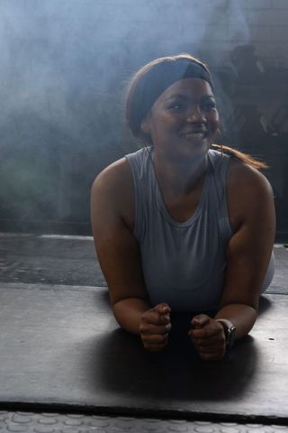 African american woman smiling during forearm plank workout in moody gym with headband
