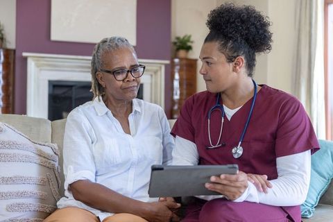 Senior african american woman consulting male nurse on tablet in cozy living room