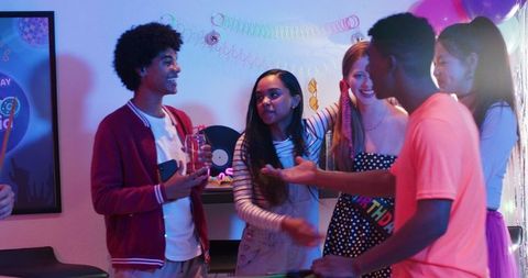 Diverse teens celebrating birthday party at home with colorful lights and casual outfits