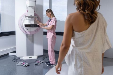 Diverse female technologist adjusting mammography machine while patient in gown waits