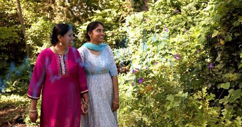 Mother and daughter walking hand in hand in sunlit garden wearing kurta and dupatta
