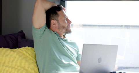 Relaxing with laptop at home, man enjoys sunny break on bright sofa