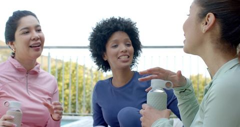 Multiracial women chatting on balcony after workout holding reusable water bottles