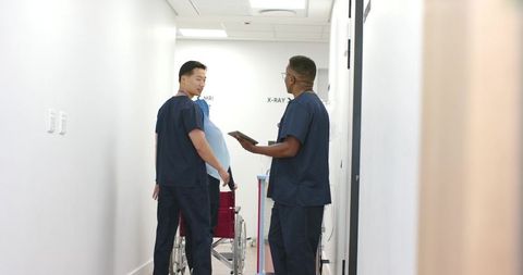 Radiology team assisting patient in wheelchair in hospital corridor while using tablet