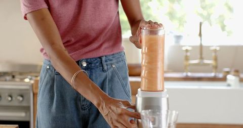 Woman mixing orange smoothie in modern kitchen for healthy lifestyle