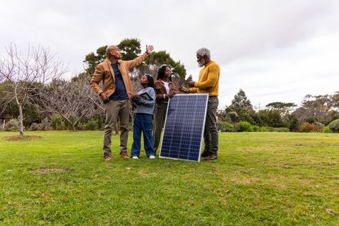 African american family discussing solar panel use in park with senior demonstrating tech