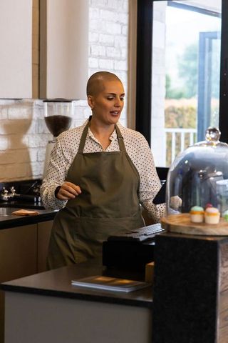 Middle-aged barista using pos at cafe counter with pastry dome and cupcakes