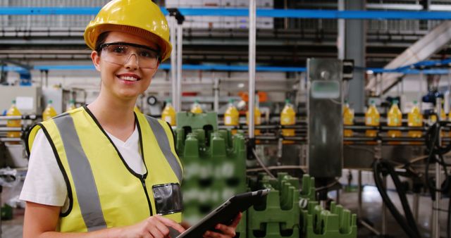 Female factory worker wearing hard hat and safety vest smiling while holding tablet - Download Free Stock Images Pikwizard.com